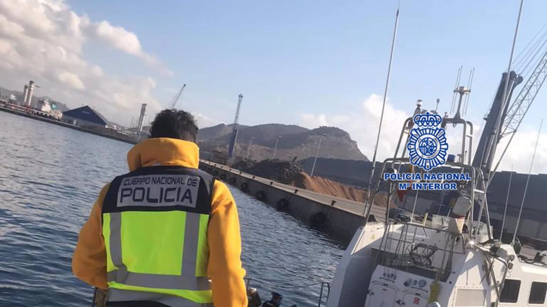 Un agente observa un barco en el que se encuentran varias personas inmigrantes