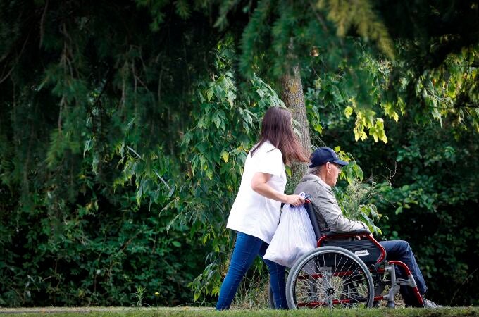 Una mujer pasea con un hombre en silla de ruedas