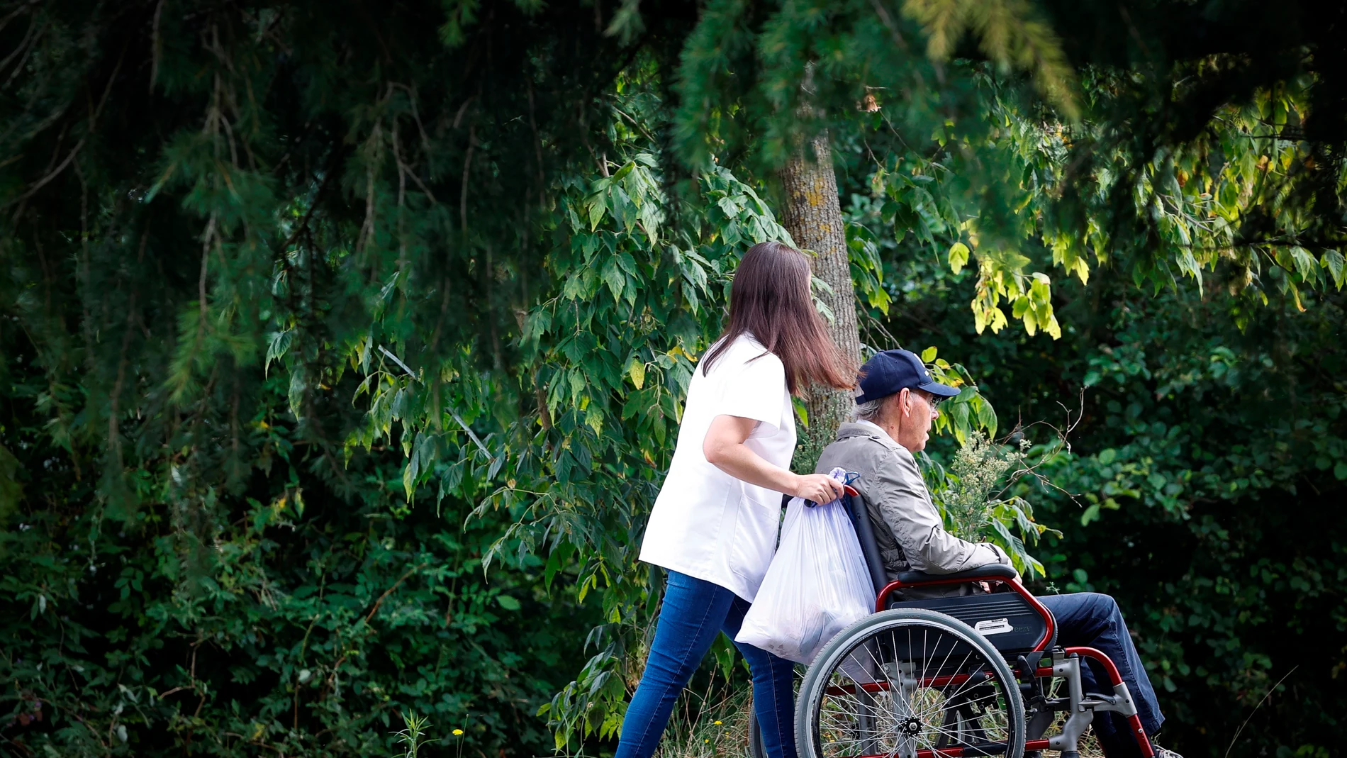 Una mujer pasea con un hombre en silla de ruedas