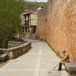 Una mujer descansa en un banco junto a las murallas de Covarrubias (Burgos)
