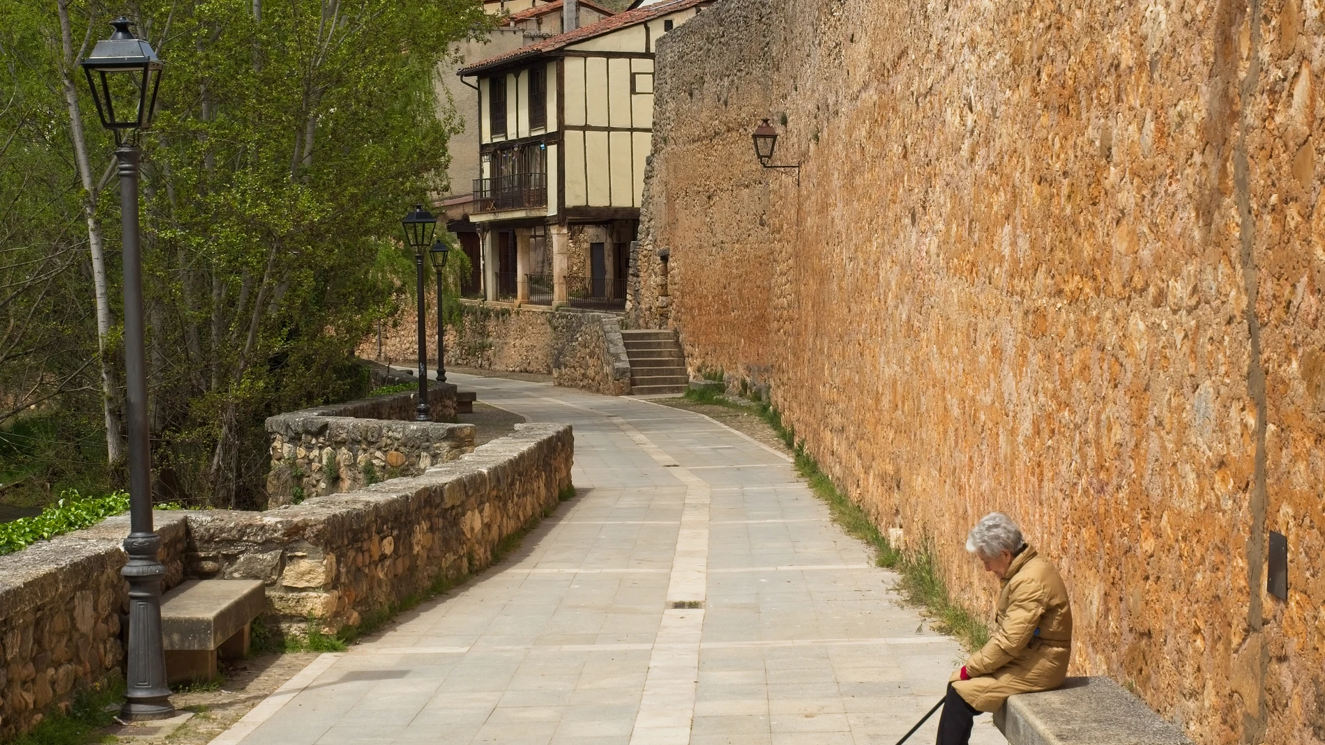 Una mujer descansa en un banco junto a las murallas de Covarrubias (Burgos)