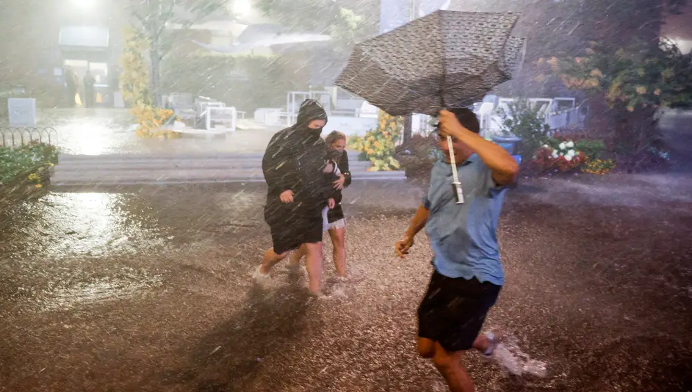 Varias personas trata de caminar en medio de las fuertes lluvias y los pasillos inundados en el Centro Nacional de Tenis Billie Jean King en la zona de Flushing Meadows, Nueva York.