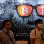 Dos hombres pasan junto a un cartel publicitario de Bitcoins y criptomonedas en Hong Kong
