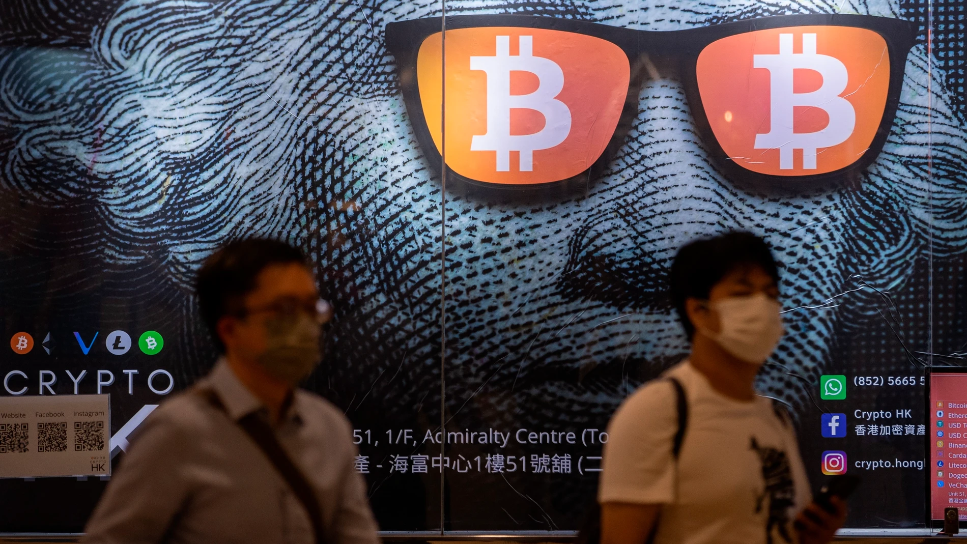 Dos hombres pasan junto a un cartel publicitario de Bitcoins y criptomonedas en Hong Kong
