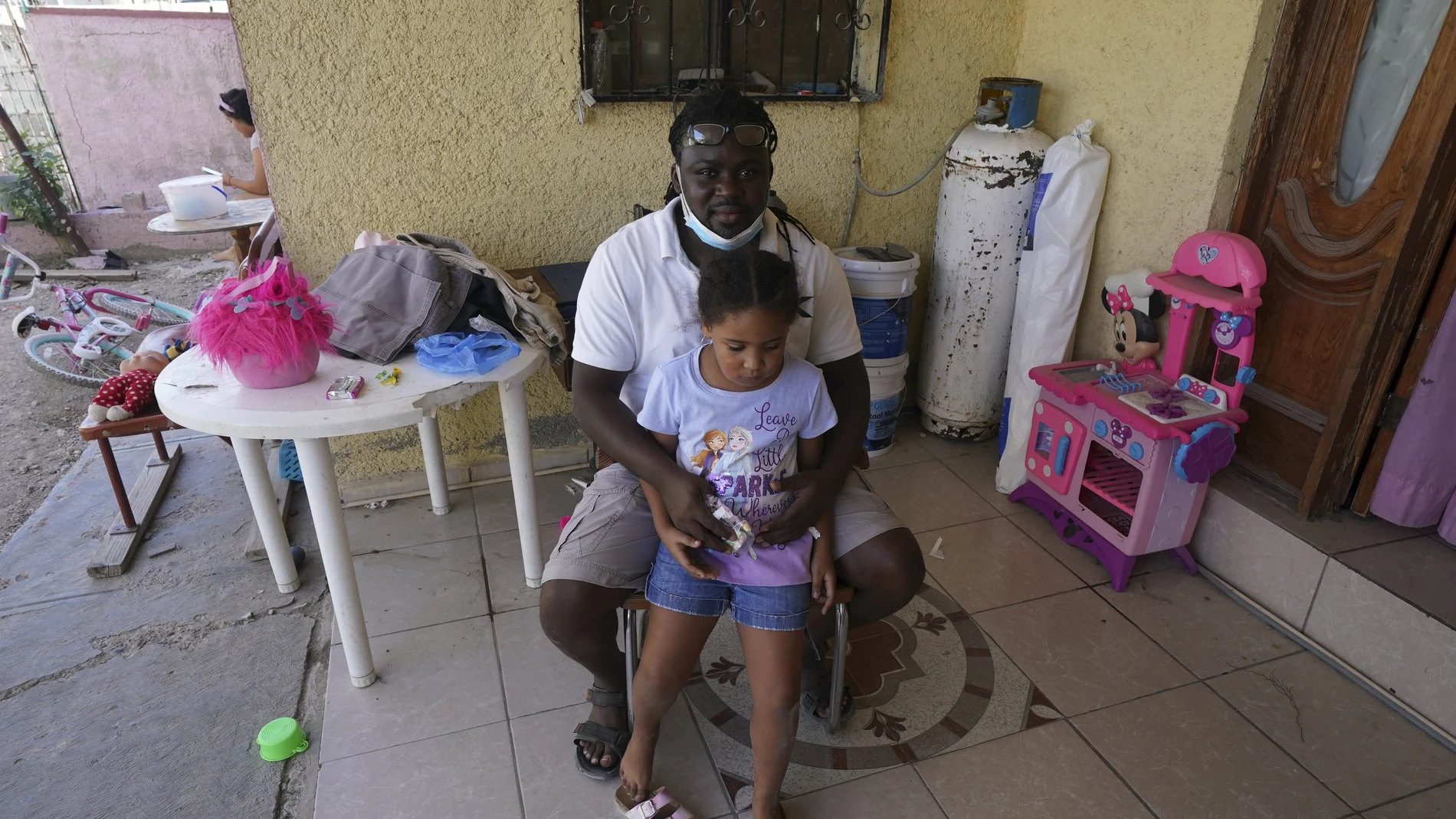 Mensah Montant and his daughter Rachel sit on their porch in Ciudad Acuna, Friday, Sept. 24, 2021. Montant, from the African nation of Togo, and his wife, are among the Acuna residents who are responding to the needs of Haitian migrants. (AP Photo/Fernando Llano)