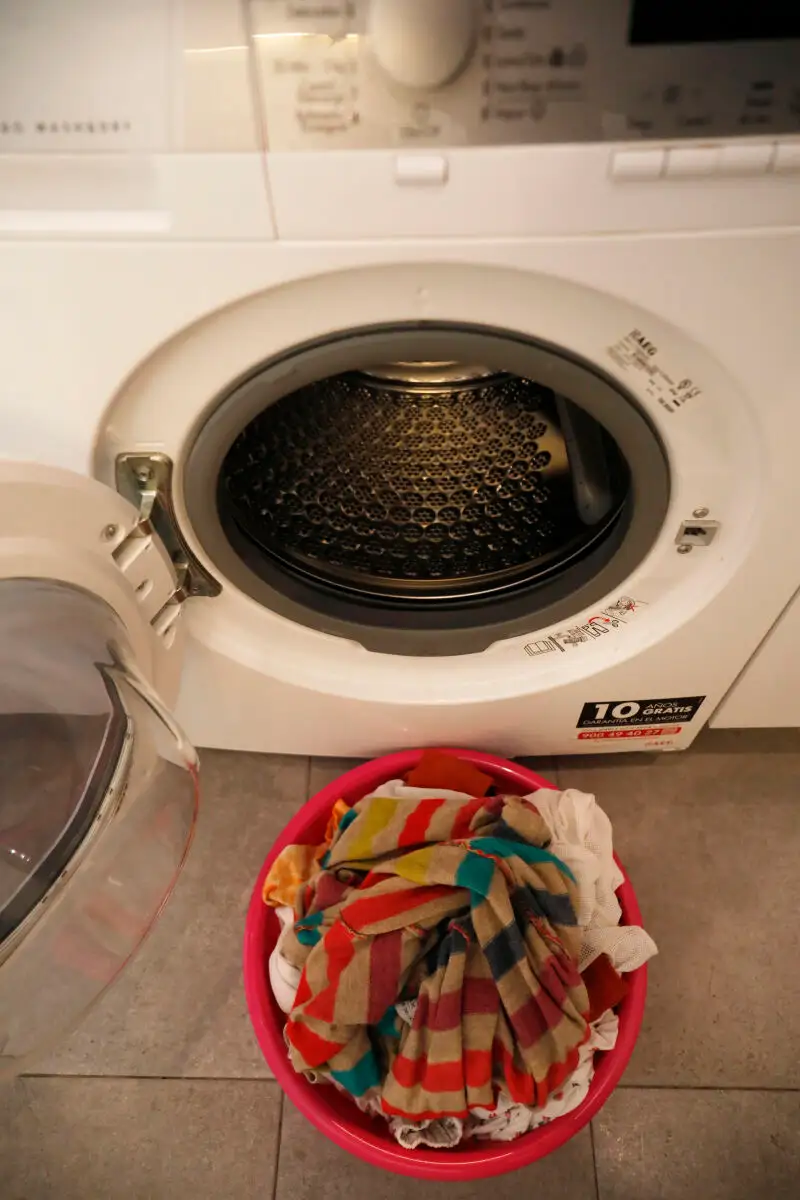 Un barreño con ropa sucia frente a una lavadora.