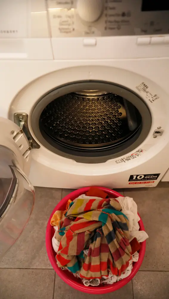 Un barreño con ropa sucia frente a una lavadora.