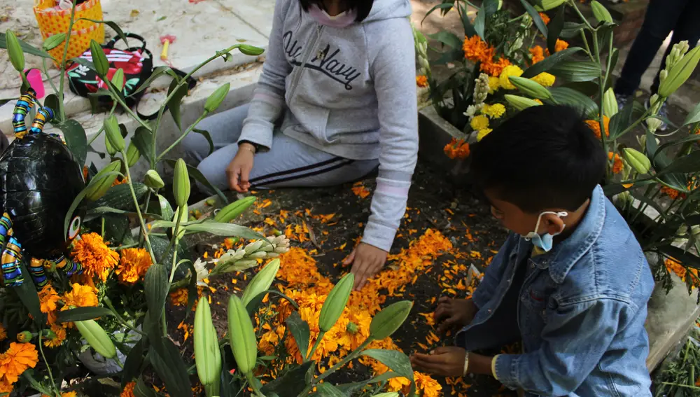 Germán Capultitla y su hermana mayor decoran las tumbas de su tía María Guadalupe y su abuela Flora con una cruz de pétalos de cempasúchil, la flor tradicional del Día de Muertos, en el cementerio de Xilotepec en el sur de Ciudad de México.