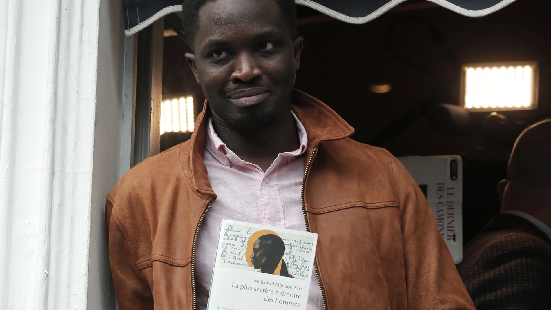 El novelista Mohamed Mbougar Sarr sostiene una copia de su libro en el balcón del restaurante parisino de Drouant
