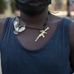 A man wearing a necklace adorned with charms depicting a phoenix and a machine gun, waits for faithful to exit the Saint Peter's Catholic church to beg for alms, in Port-au-Prince, Haiti, Tuesday, Sept. 28, 2021. (AP Photo/Rodrigo Abd)