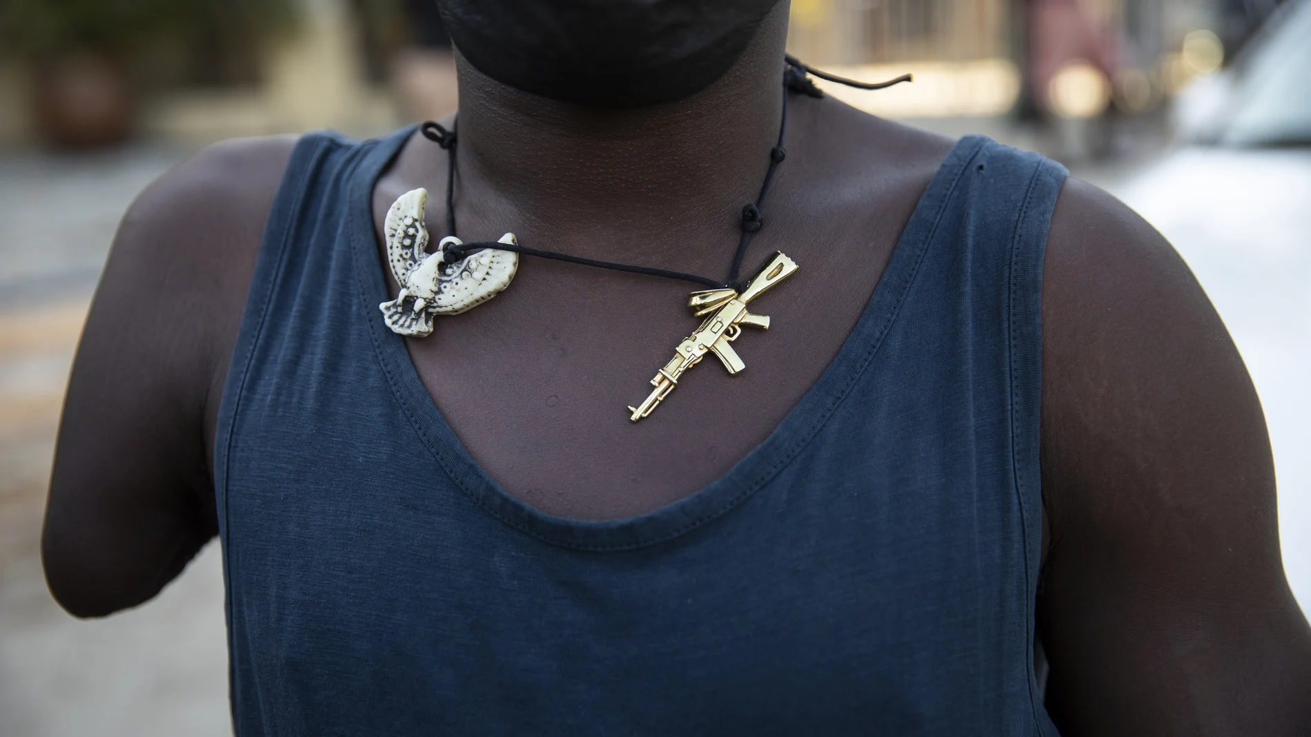 A man wearing a necklace adorned with charms depicting a phoenix and a machine gun, waits for faithful to exit the Saint Peter's Catholic church to beg for alms, in Port-au-Prince, Haiti, Tuesday, Sept. 28, 2021. (AP Photo/Rodrigo Abd)