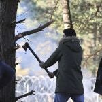 Un hombre tala un árbol para tratar de romper la valla de púas de la frontera polaca