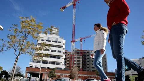 Dos jóvenes pasan por delante de un edificio de viviendas en construcción