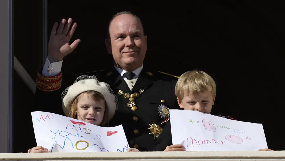 Prince Albert II of Monaco waves as his children Prince Jacques and Princess Gabriella show messages for their mother Princess Charlene, from the balcony of the the Monaco Palace during ceremonies marking National Day, Friday Nov.19, 2021 in Monaco. Princess Charlene is currently convalescing in a confidential place after battling with poor health over the past few months. (AP Photo/Daniel Cole)