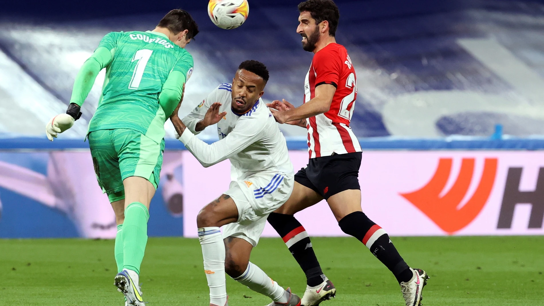 El guardameta belga del Real Madrid, Thibaut Courtois (i), despeja el balón ante su compañero, el brasileño Militao y el delantero del Athletic Club, Raúl García (d), durante el encuentro de LaLiga