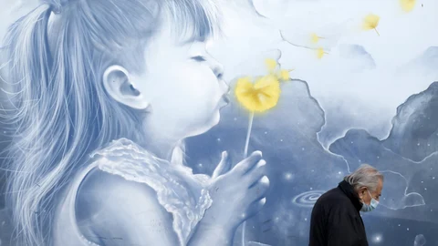 Un peatón con una máscara facial para protegerse contra el coronavirus, camina frente a un mural, en una estación de metro en Atenas, Grecia