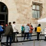 Varias personas hacen cola ante el punto de vacunación sin cita previa instalado ante la puerta del palcaio de la Generalitat Valenciana