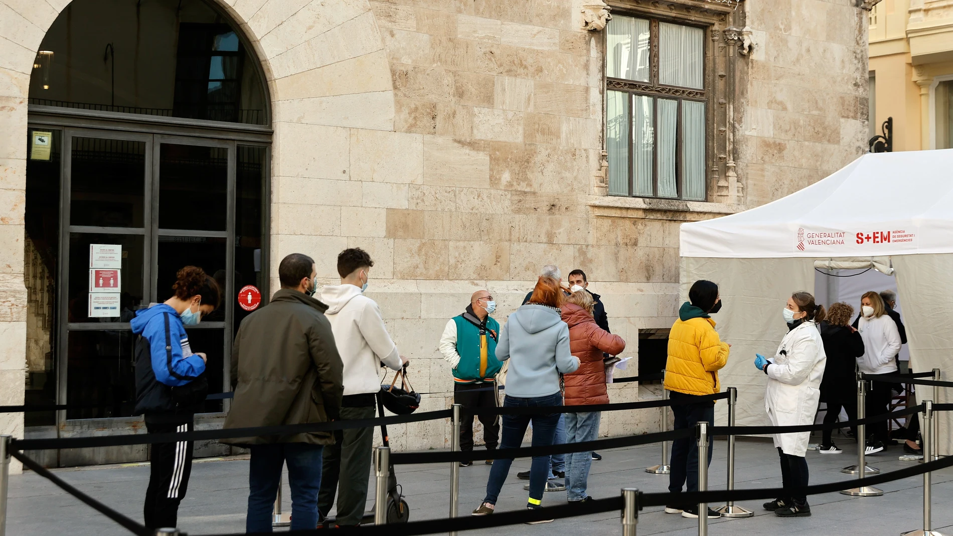 Varias personas hacen cola ante el punto de vacunación sin cita previa instalado ante la puerta del palcaio de la Generalitat Valenciana