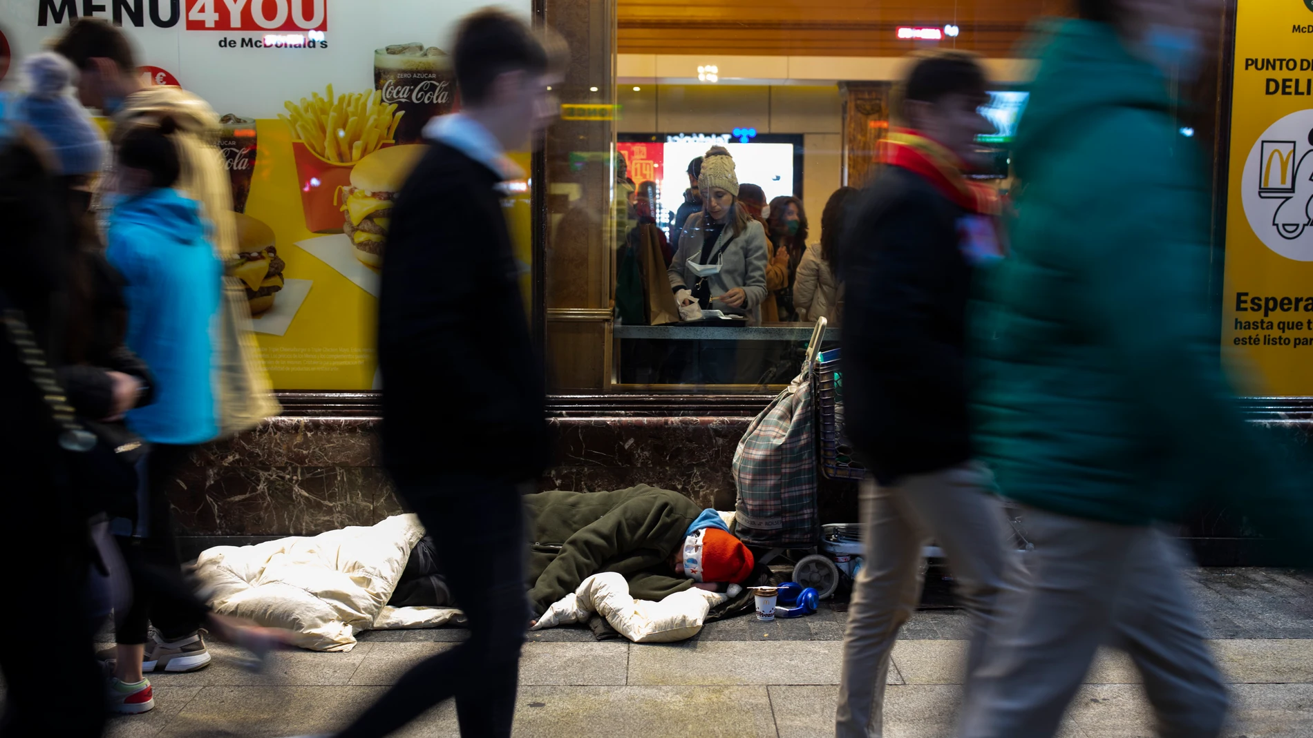 Imagen de una persona sin hogar durmiendo en la puerta de un McDonald's en Gran Vía.