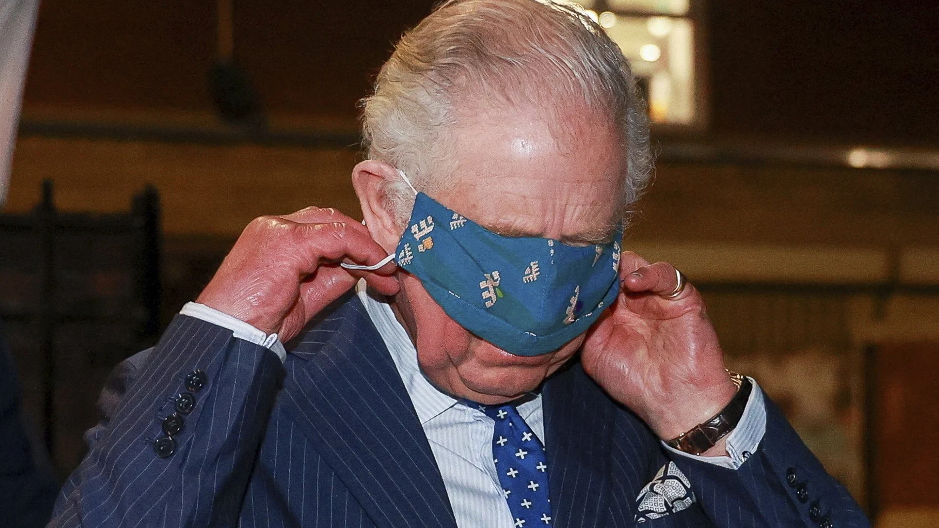 El príncipe Carlos ajustándose con notables dificultades su mascarilla durante un acto público en Londres