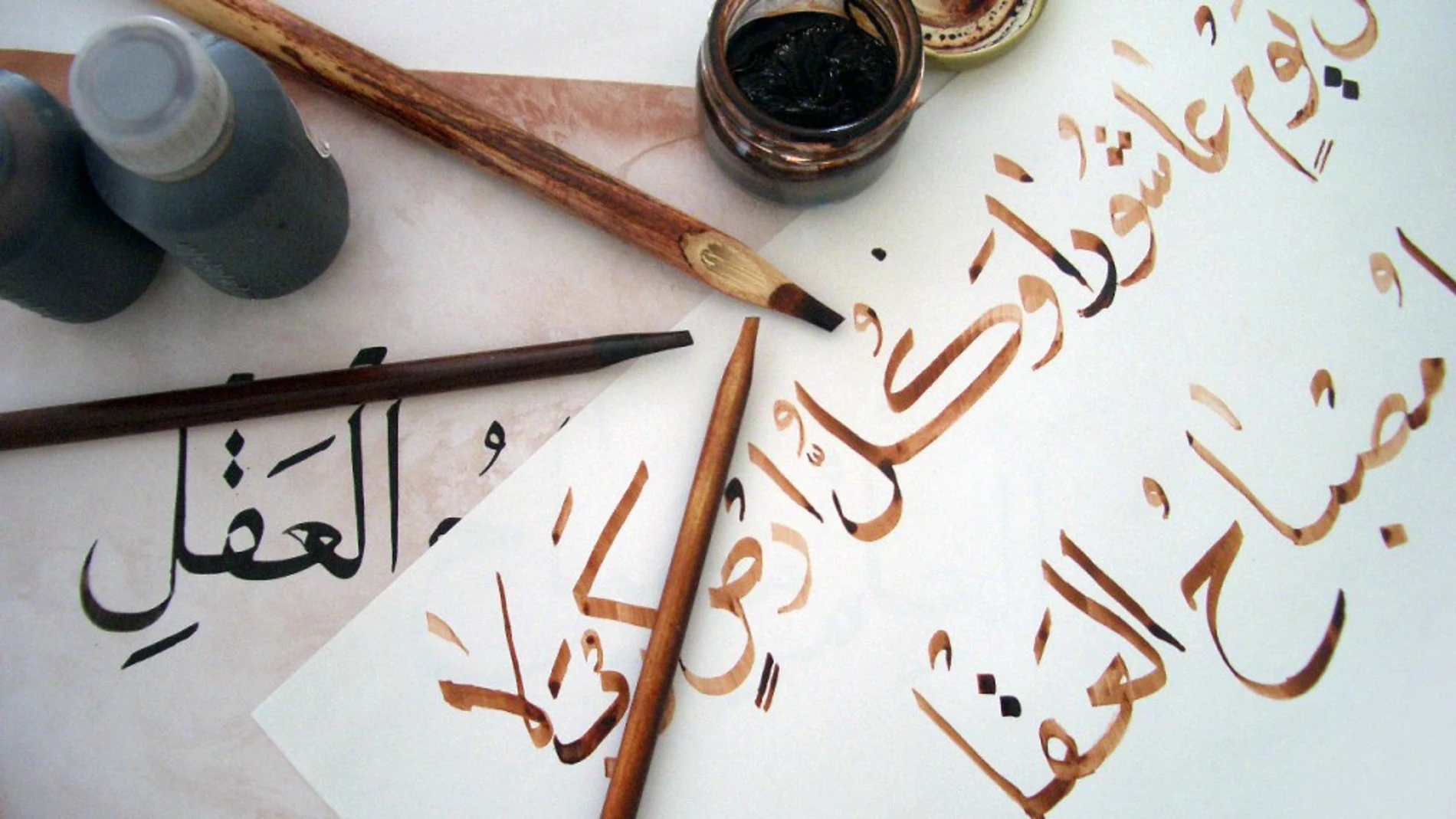 Obra de un estudiante de caligrafía árabe, utilizando bolígrafos de bambú y tinta marrón, trazando sobre la obra del profesor con tinta negra.