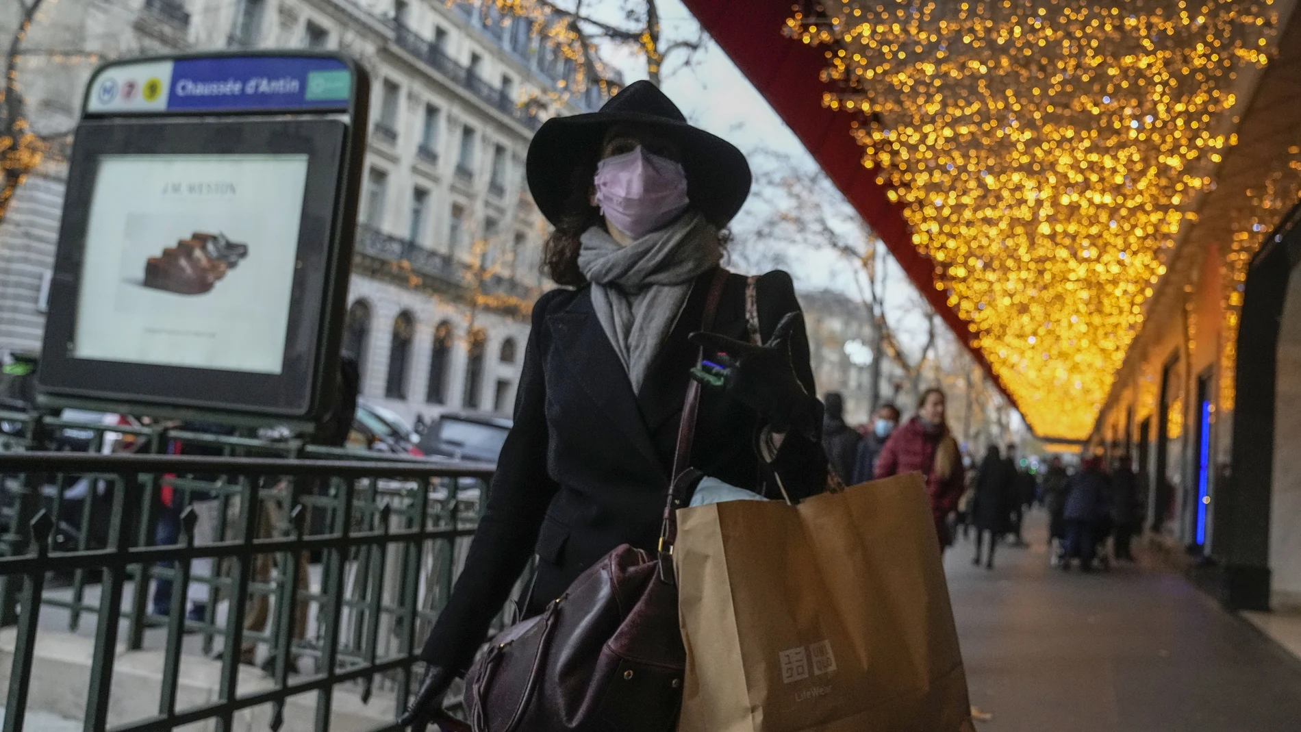 Una mujer protegida con una mascarilla camina con una bolsa con compras en una calle de París
