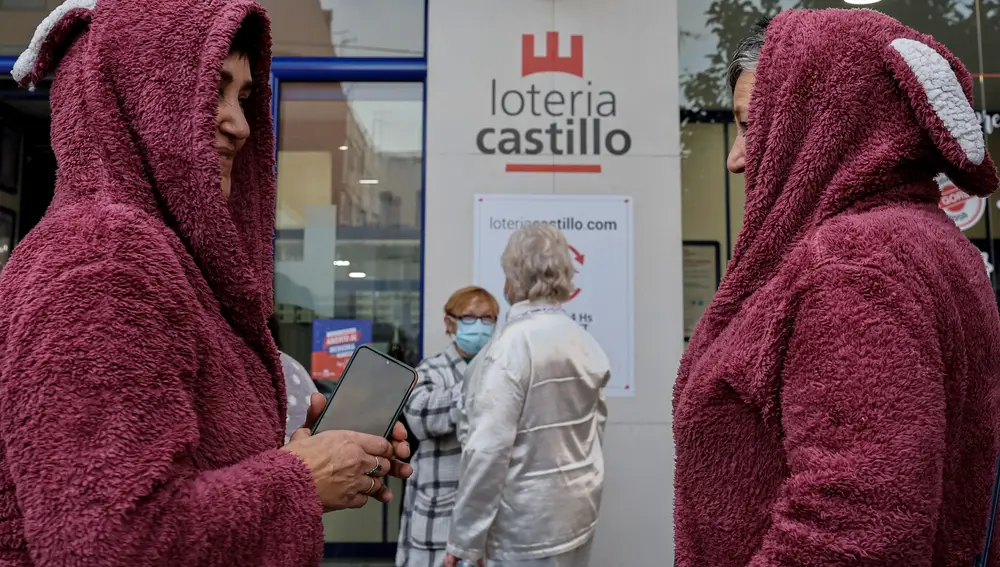 GRAFCVA1699. ALAQUÀS (VALENCIA), 21/12/2021.- Varias personas acuden a una administración de lotería de Alaquàs (Valencia), que regala décimos del sorteo de Navidad a los 50 primeros clientes que lleguen en pijama. EFE/Biel Aliño