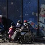 Residents enjoy the sun near a display promoting winter sports on New Year's Eve in Beijing, China, Friday, Dec. 31, 2021. (AP Photo/Ng Han Guan)