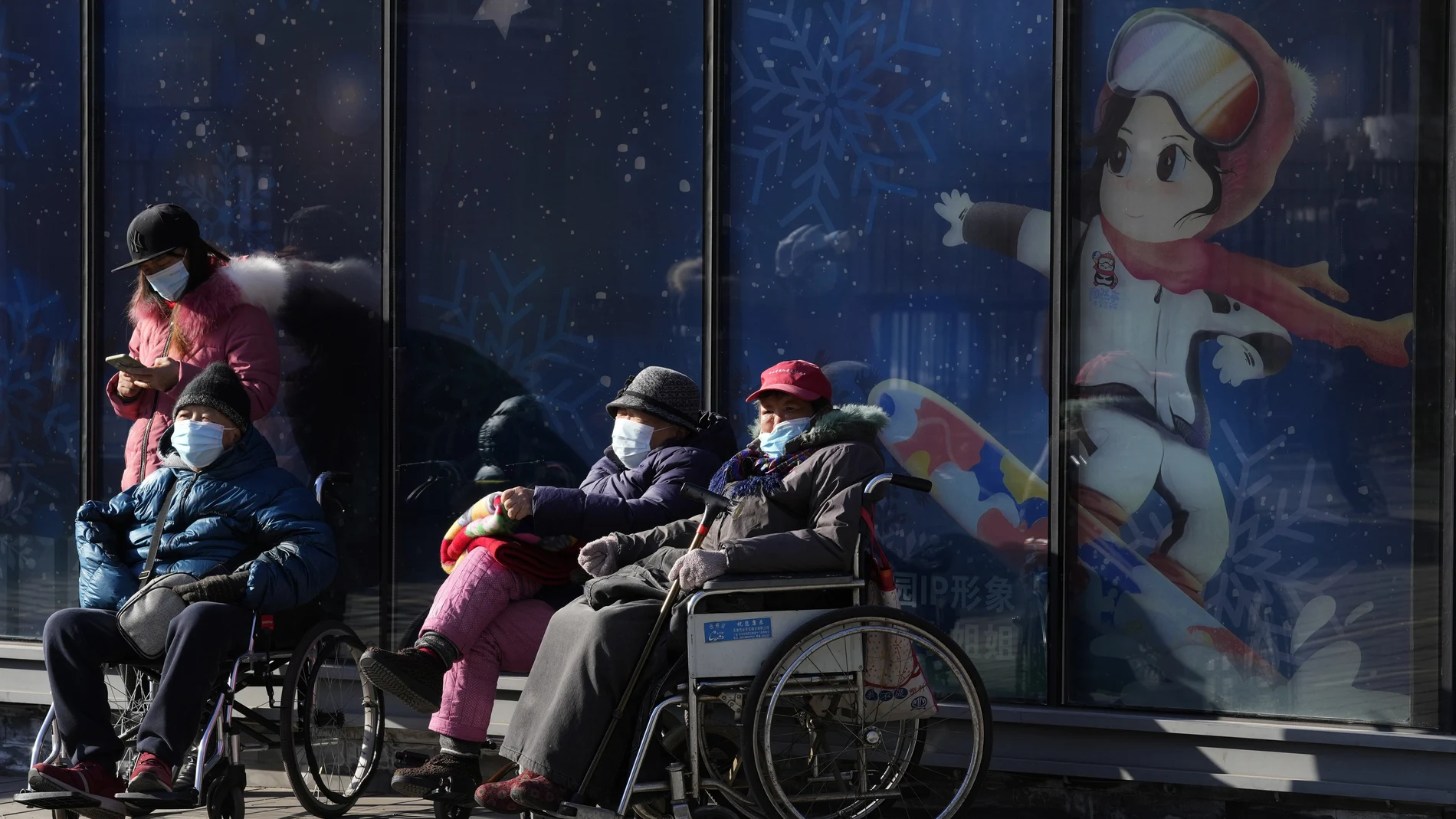 Residents enjoy the sun near a display promoting winter sports on New Year's Eve in Beijing, China, Friday, Dec. 31, 2021. (AP Photo/Ng Han Guan)