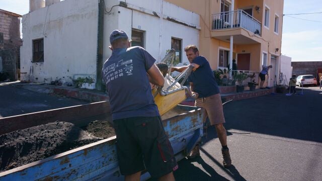 Dos hombres limpian de ceniza volcánica el frente de una vivienda en el municipio palmero de Tazacorte