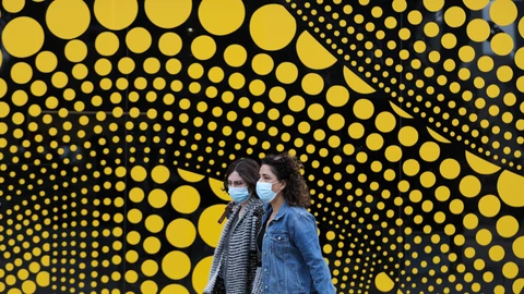 Unas mujeres con mascarillas pasan delante de un centro de recogida de muestras para la detección de casos de coronavirus al lado del Museo de Tel Aviv en Tel Aviv, Israel