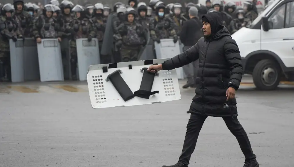 Un manifestante lleva un escudo policial frente a la línea policial durante una protesta en Almaty