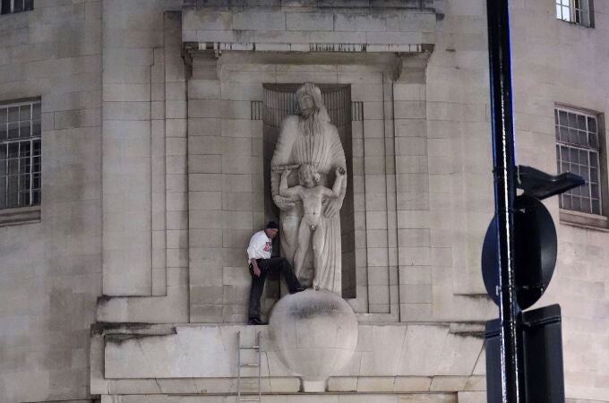 A man, after climbing a ladder, stands next to the statue of Prospero and Ariel from Shakespeare's play The Tempest by the sculptor Eric Gill outside the BBC's Broadcasting House in central London, Wednesday Jan. 12, 2022. British police have cordoned off an area outside the BBC in central London after a man was spotted scaling the building and using a hammer to attack a statue by controversial sculptor Eric Gill.