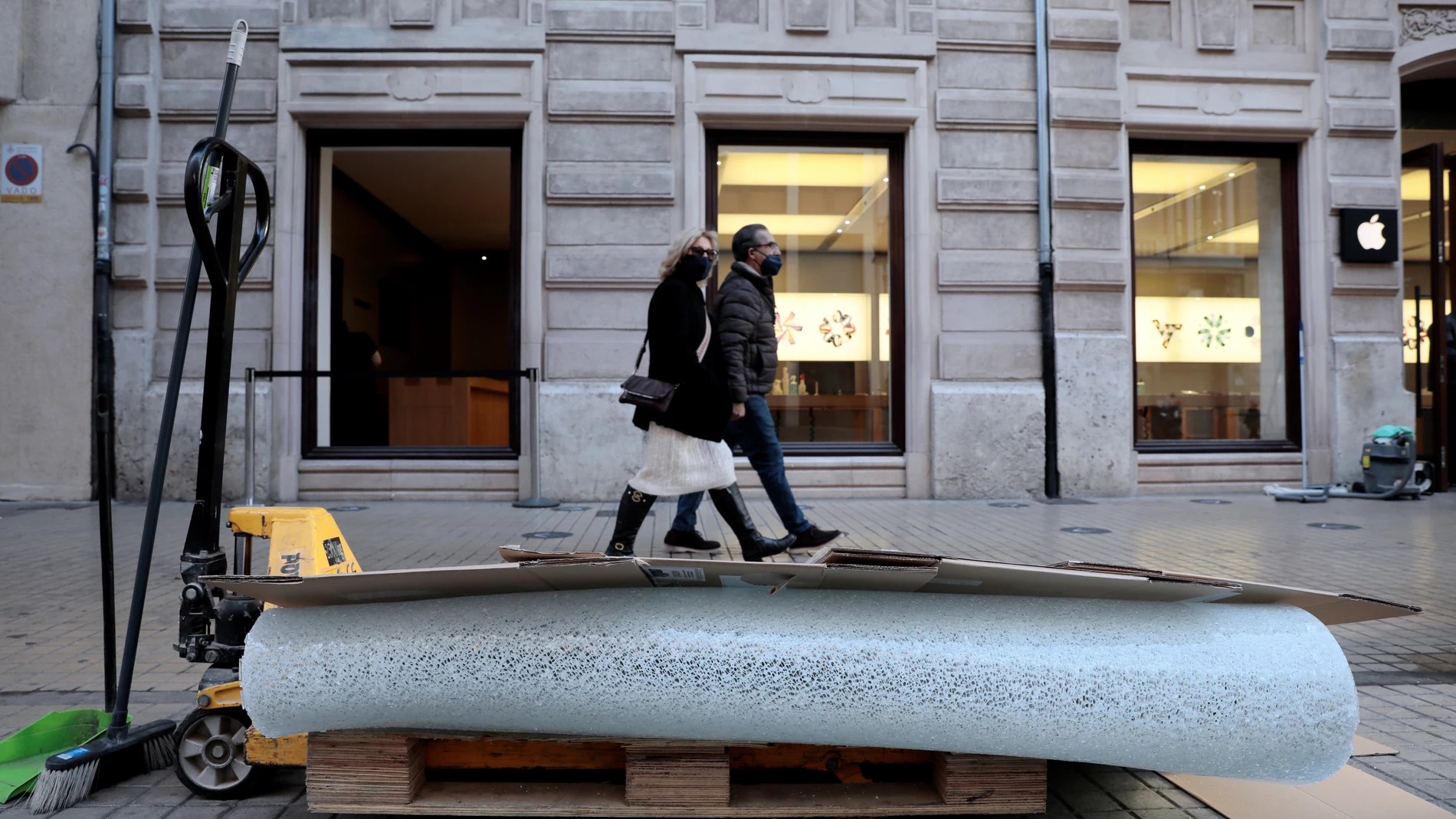 Dos personas pasan junto al cristal roto y ante la tienda Apple ubicada en la calle Colón, en pleno centro de València