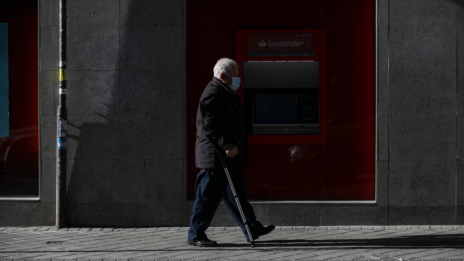 Una persona mayor pasa frente a un cajero del Banco Santander
