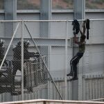 Dos agentes se acercan a un migrante que intenta saltar la valla que separa Ceuta de Marruecos.
