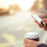 Una persona mira su móvil mientras toma un café