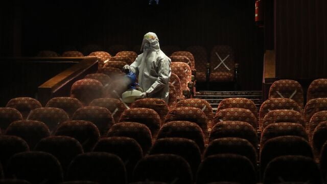 Un empleado sanitario desinfecta los asientos de una sala de cine