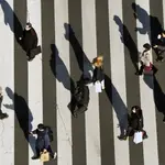 Personas que usan mascarillas protectoras contra la Covid-19 caminan por un paso de peatones el lunes 31 de enero de 2022 en Tokio
