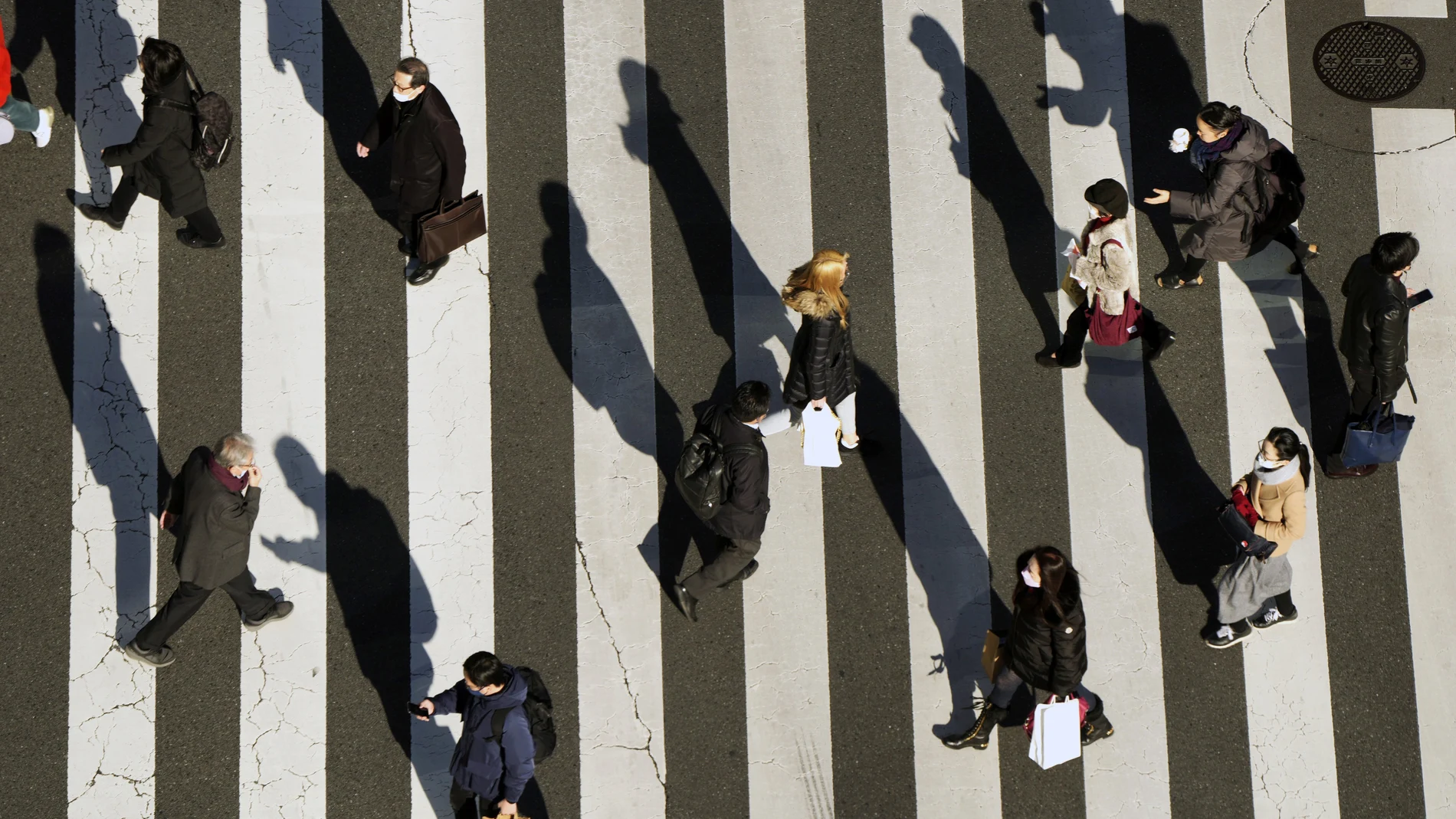 Personas que usan mascarillas protectoras contra la Covid-19 caminan por un paso de peatones el lunes 31 de enero de 2022 en Tokio