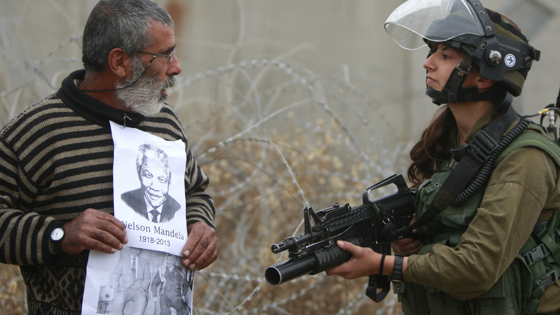 Un manifestante palestino muestra una foto de Nelson Mandela a un soldado israelí en Cisjordania