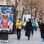 Varias personas pasan ante carteles promocionales a lo largo de una de las principales calles de Granada que acoge la Copa del Rey de Baloncesto. EFE/Miguel Ángel Molina