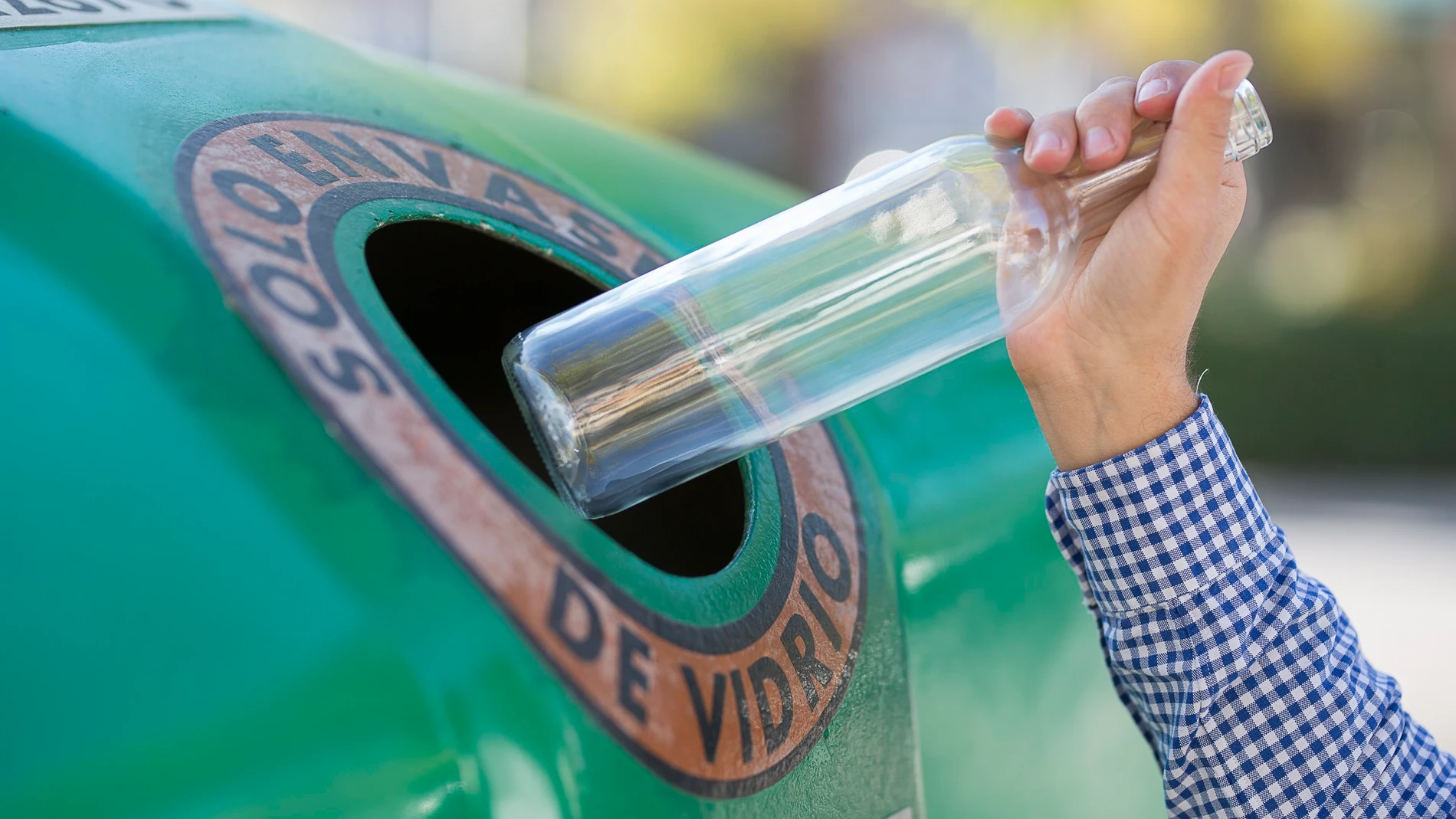 Un usuario deposita una botella de vidrio en un contenedor verde