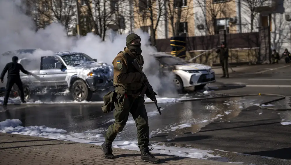 Soldados ucranianos toman posiciones fuera de una instalación militar mientras dos coches se incendian, en una calle de Kiev
