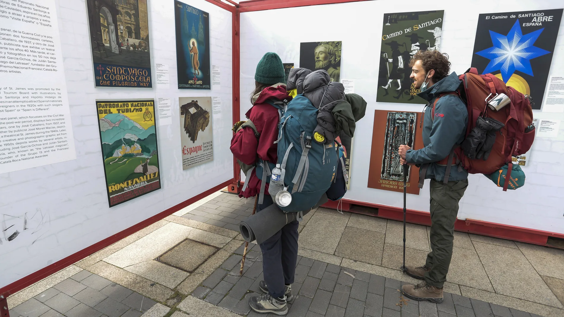 Dos peregrinos se detienen a contemplar la exposición ‘Carteles para un Camino, 100 años de Ilustración Jacobea’ en León