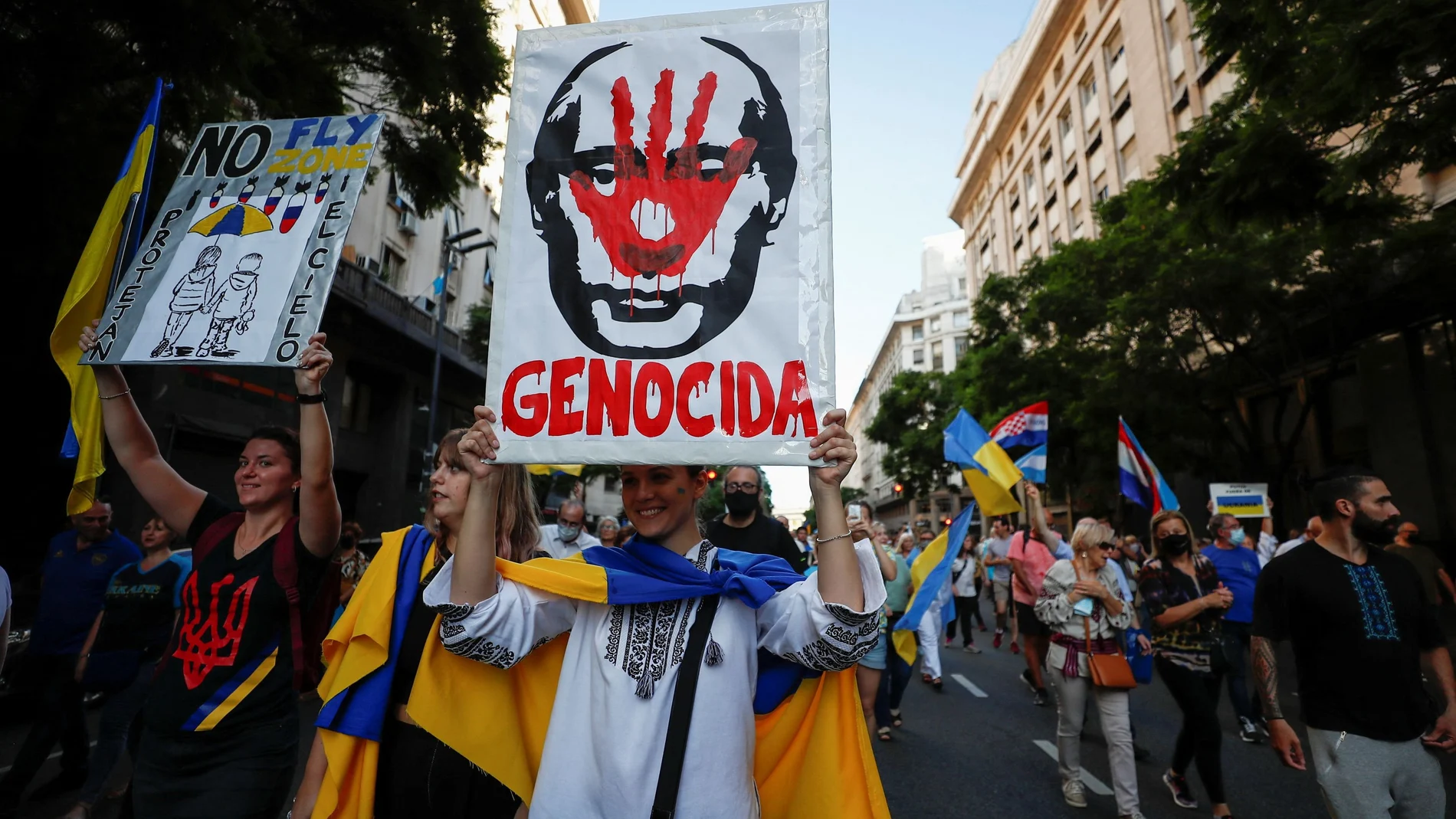 Una mujer porta un cartel con la cara de Putin y la palabra "Genocida" en medio
