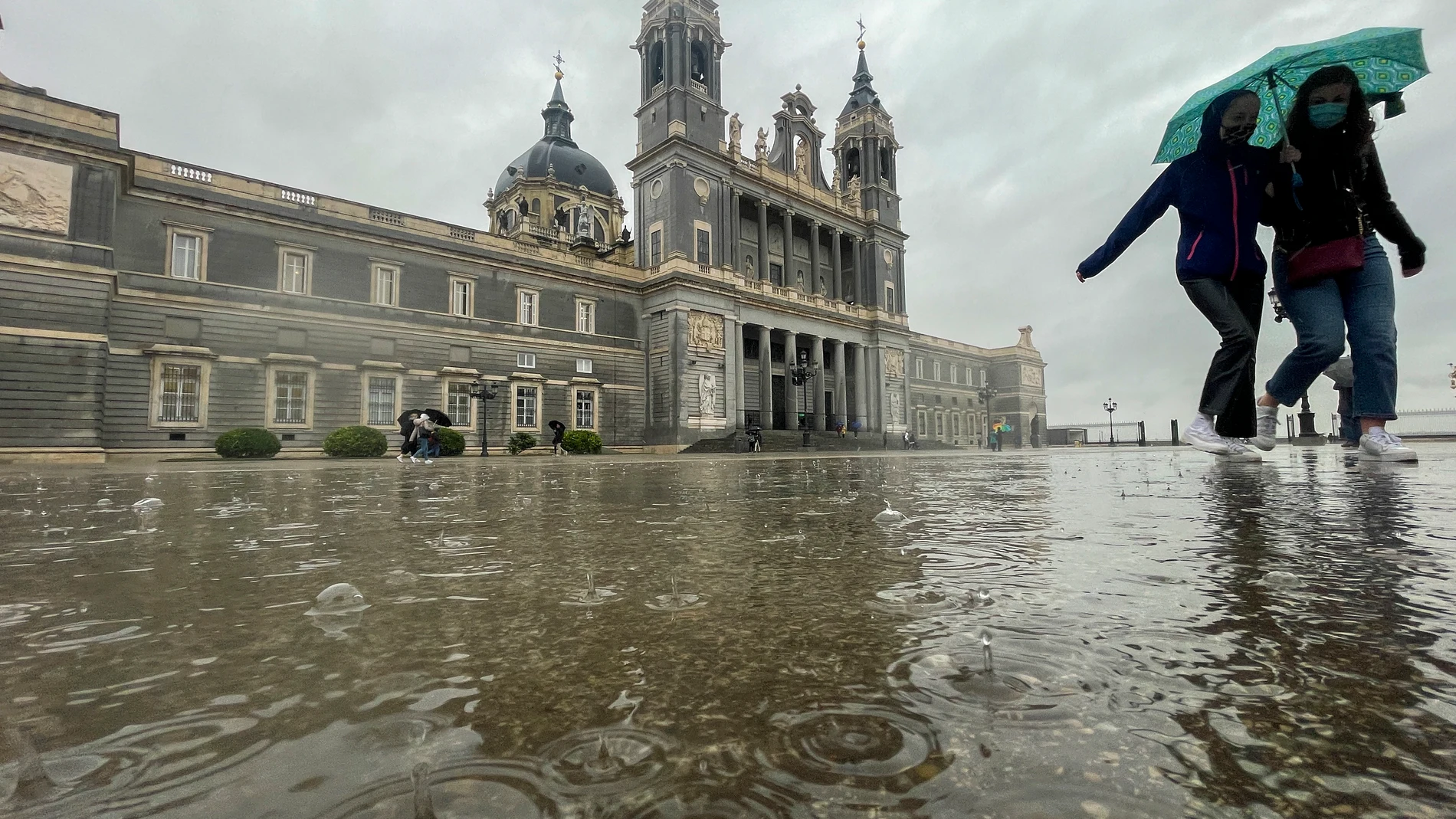 Dos mujeres caminan bajo la lluvia provocada por la borrasca Celia junto a la catedral de La Almudena en Madrid este lunes