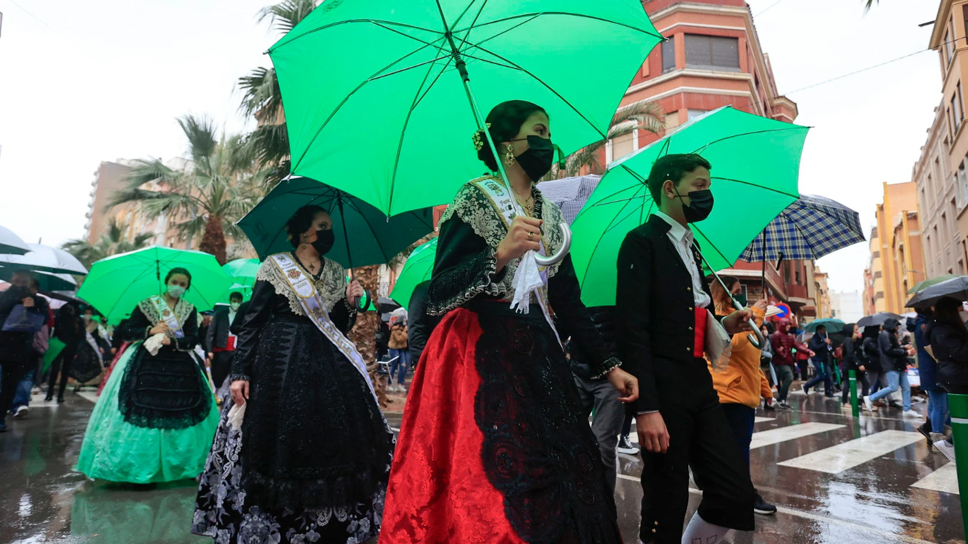 Gaiateras ataviadas con el traje tradicional se protegen de la lluvia con paraguas en la mascletà de inicio de fiestas de la Magdalena, este sábado en Castellón