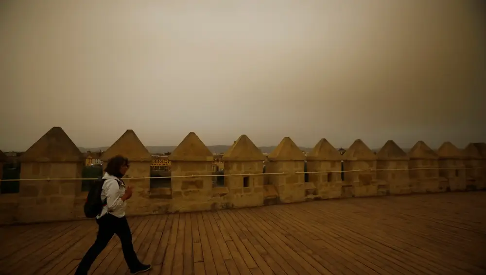Una mujer pasea por la torre de la Calahorra este jueves mientras una nube de polvo vuelve a cubrir el cielo de Córdoba