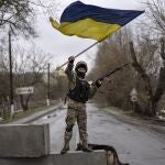 Un soldado ucraniano ondea una bandera cerca de un punto de acceso a la ciudad de Bucha